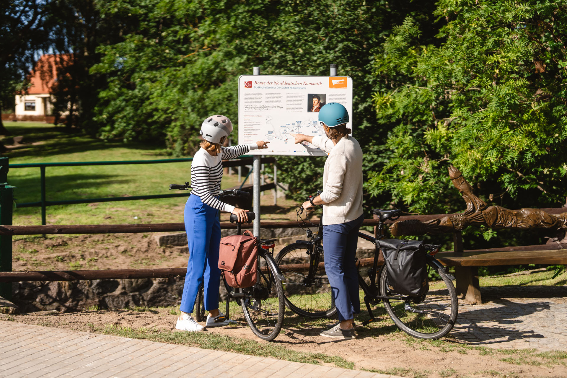 Zwei Personen mit Fahrrad stehen an der Infotafel und zeigen auf etwas.